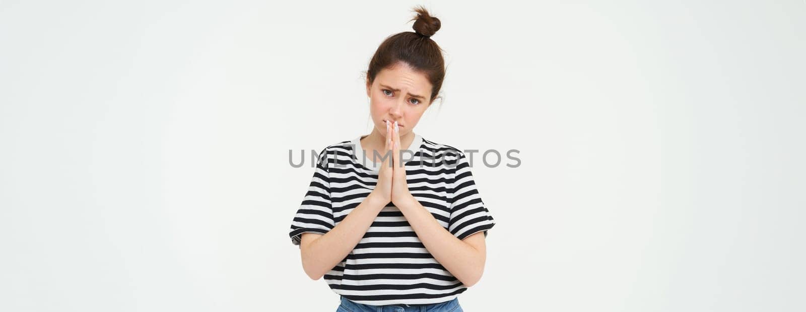 Please. Young woman asks for help, begs you, holds hands in pray, pleading, isolated against white background.