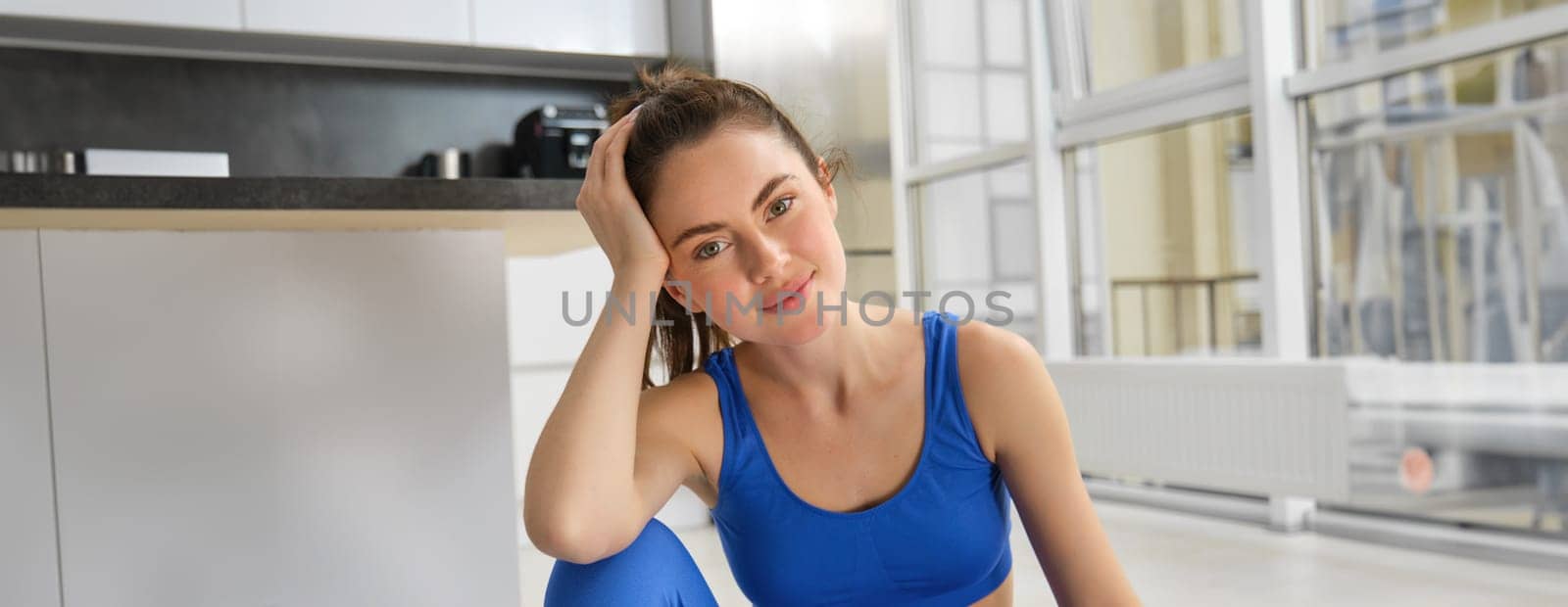 Portrait of sportswoman doing workout at home, smiling and looking at camera by Benzoix