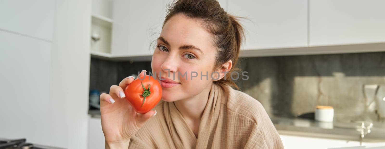 Portrait of woman cooking at home in the kitchen, holding tomatoes, preparing delicious fresh meal with vegetables, standing near chopping board by Benzoix