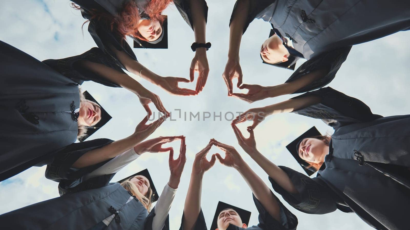 A group of college graduates stand in a circle and make hearts out of their palms