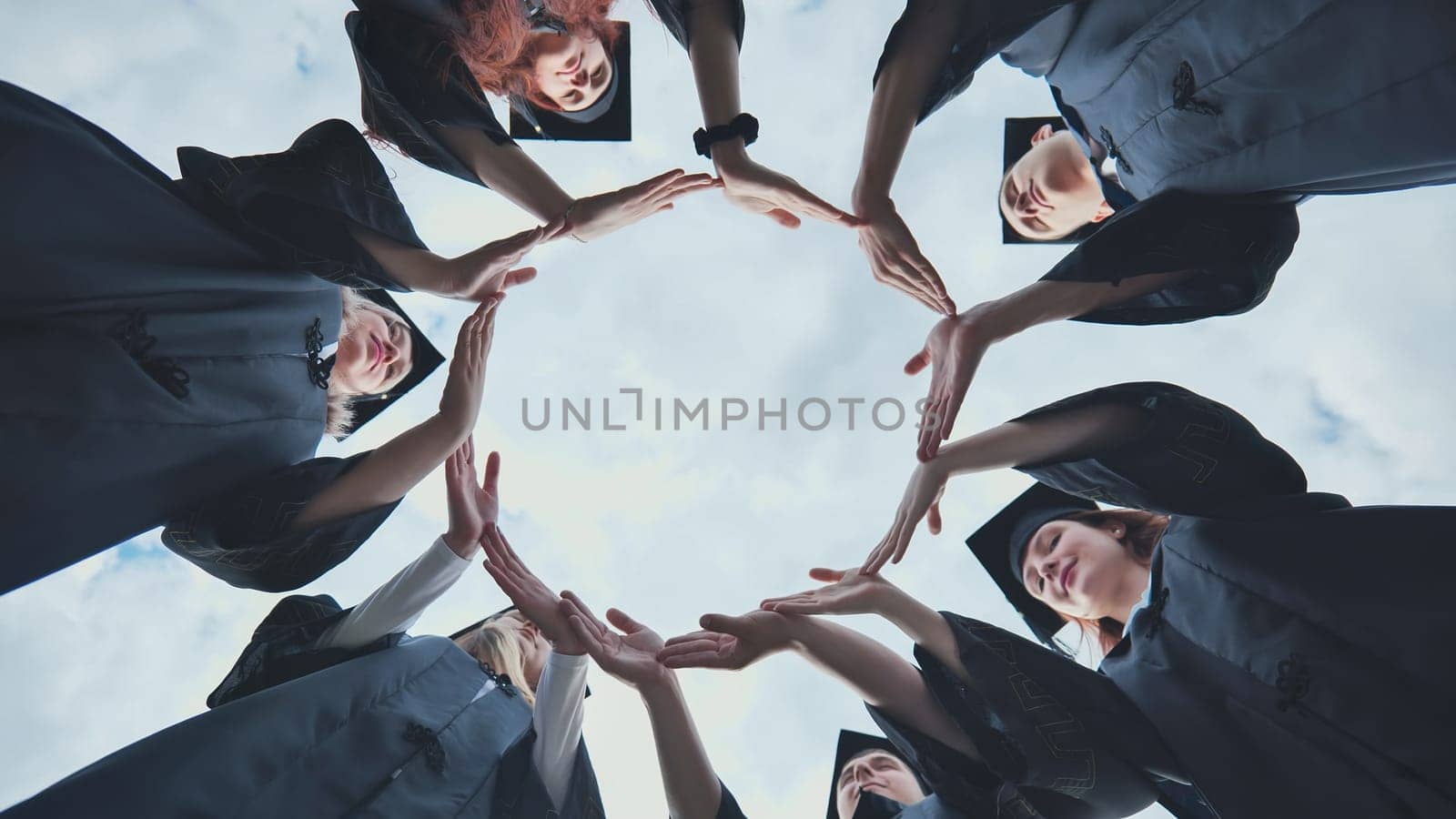 Graduate students in black robes and caps make a circle shape from their hands