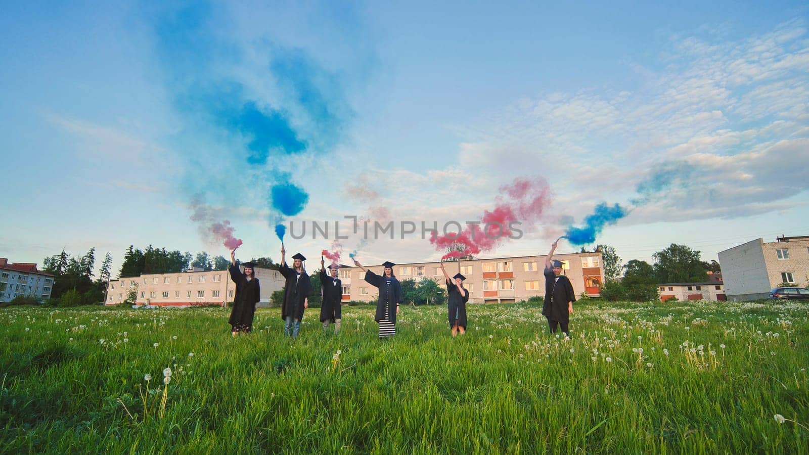 Graduates in costume walk with a smoky multi-colored smoke at sunset