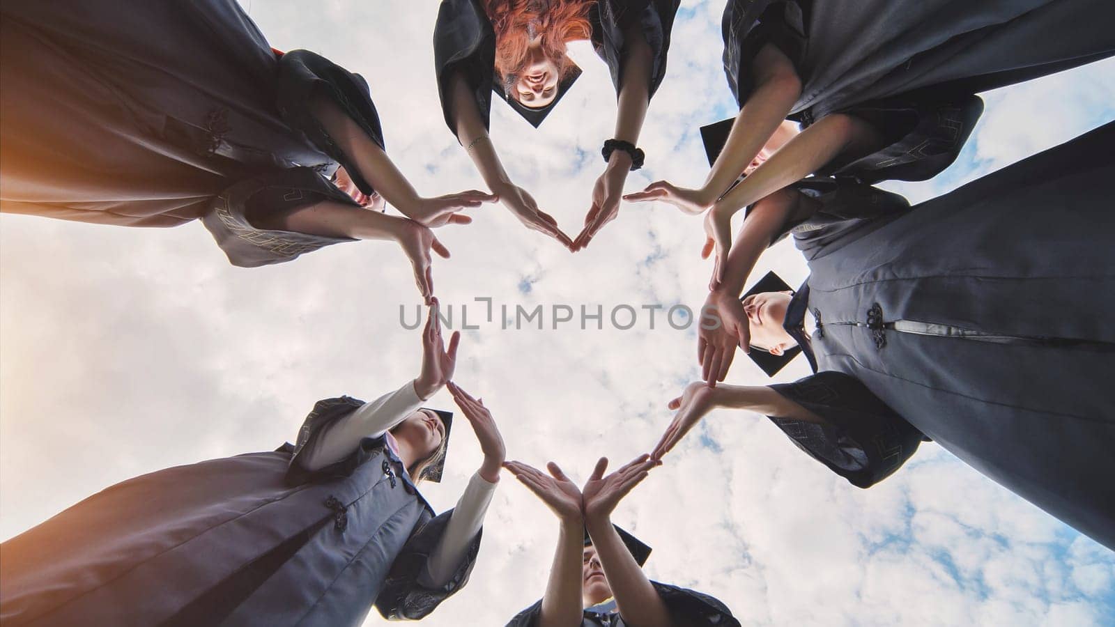 Graduates in costume make a heart shape out of their hands