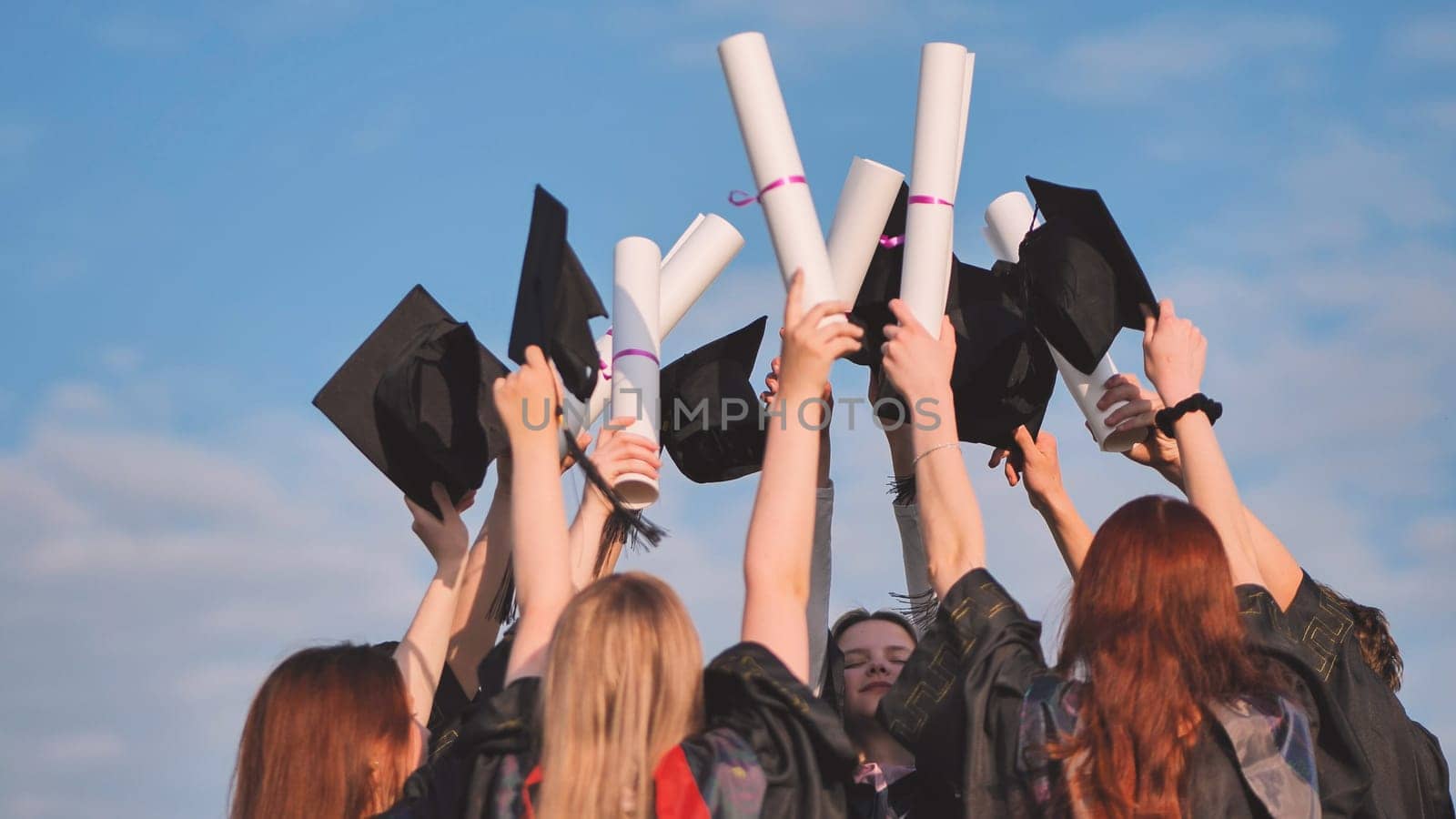 Graduates connect diplomas and caps on a sunny day. by DovidPro
