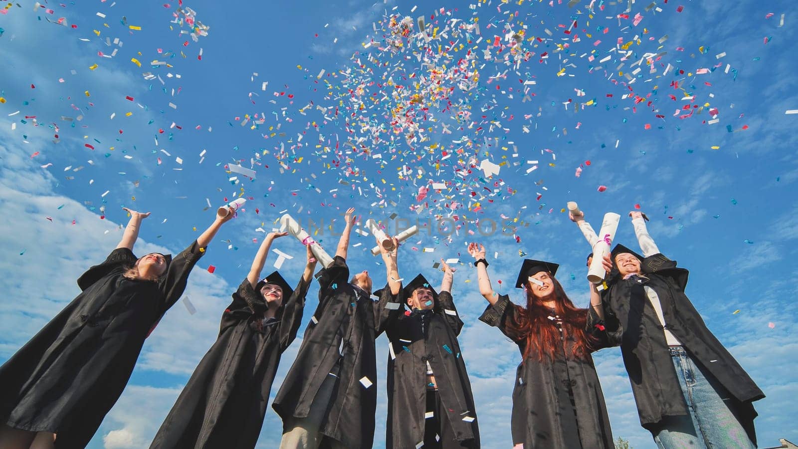 Happy graduates throwing up colorful confetti against the blue summer sky