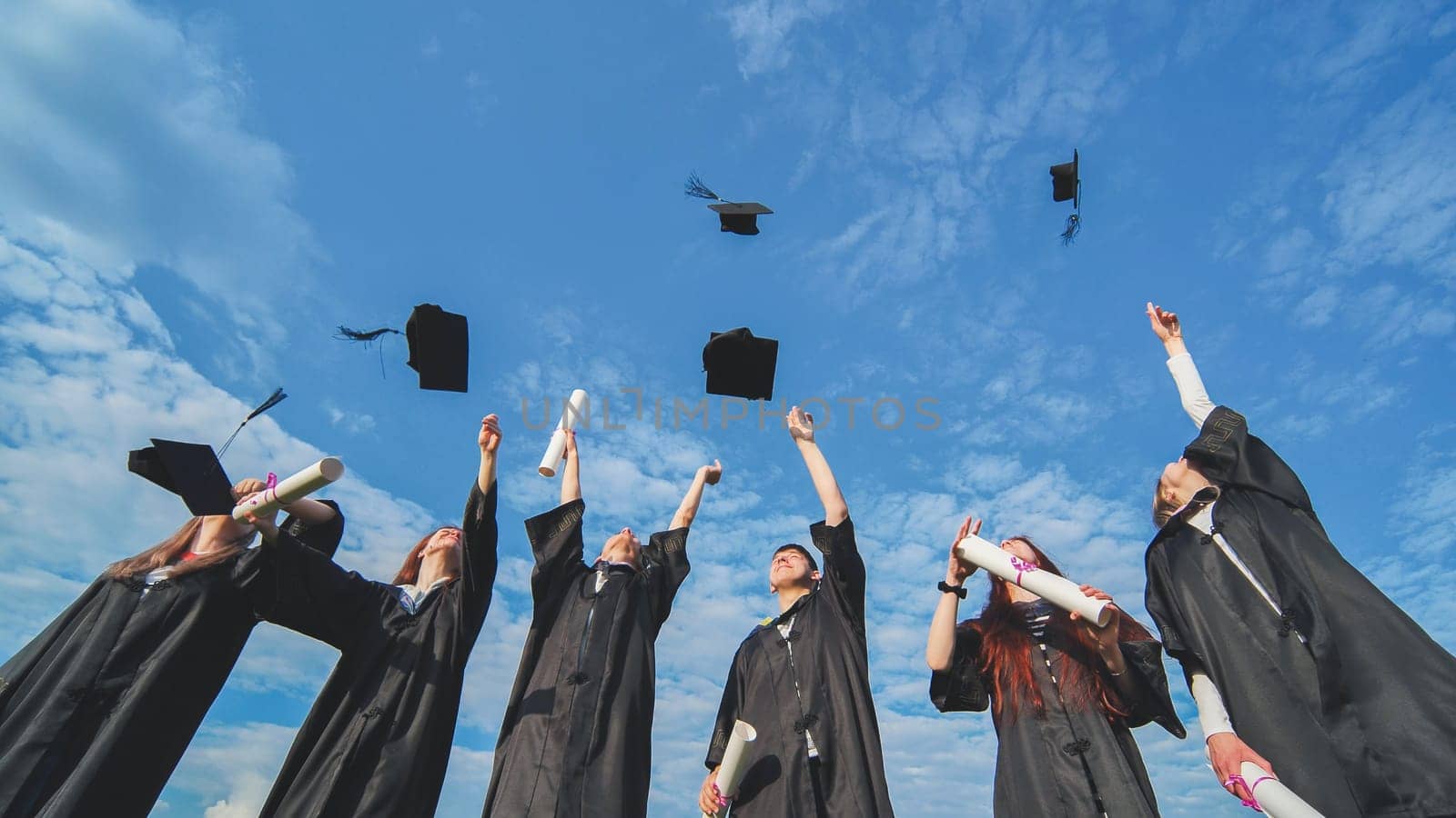Joyful graduates stand in a row and toss their caps up in the air