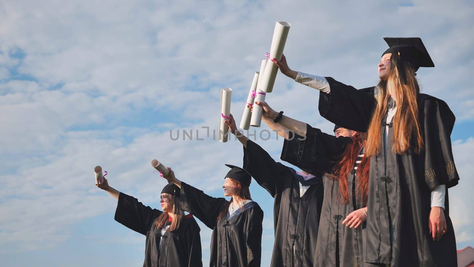 Cheerful graduates pose with raised diplomas on a sunny day