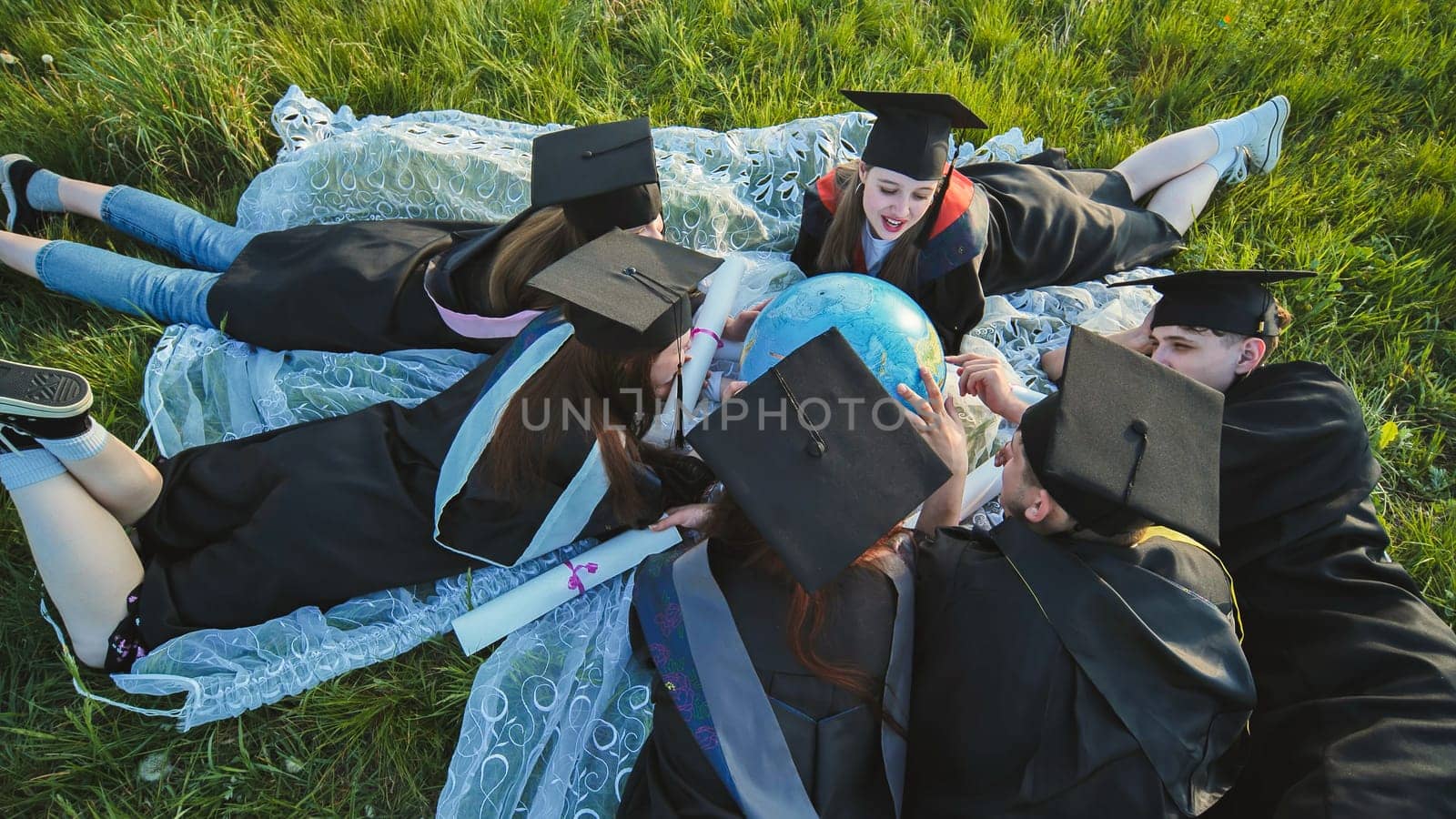 Graduates in black robes looking at a georgraphic globe lying on the grass