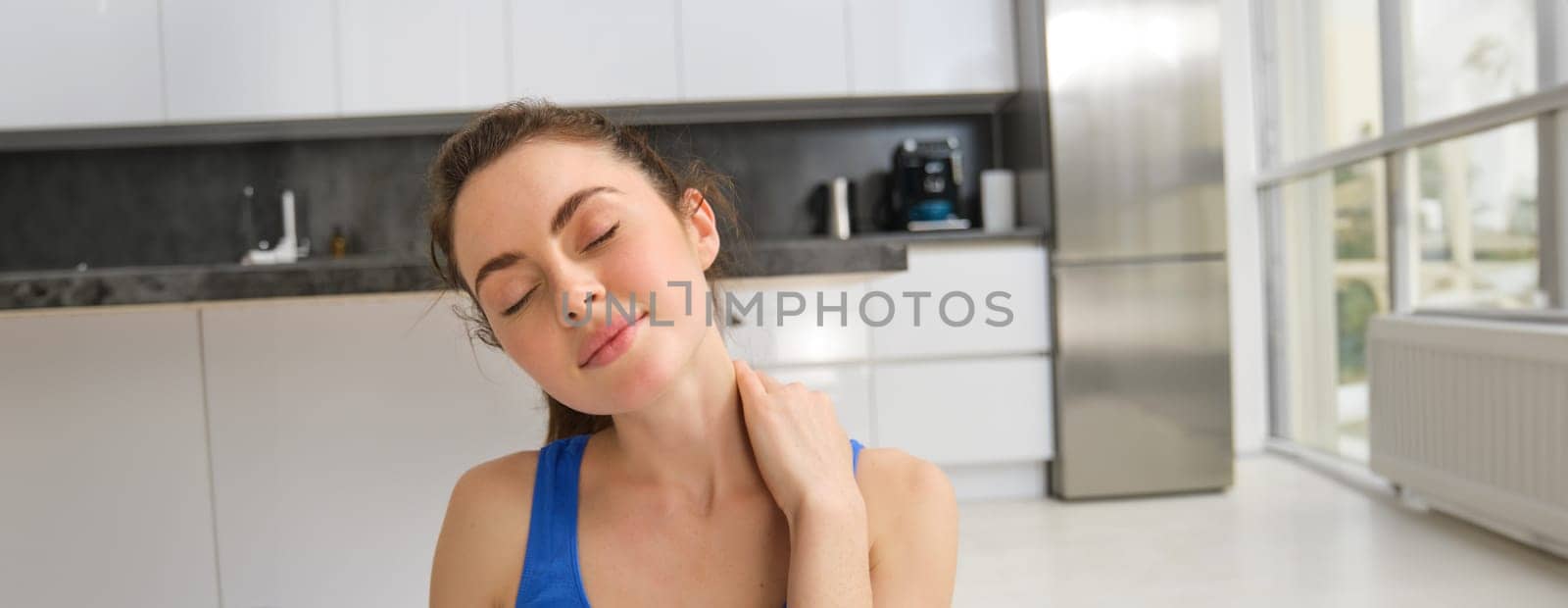 Close-up potrait of fitness woman, does training, workout from home, massaging neck, exercise in living room by Benzoix