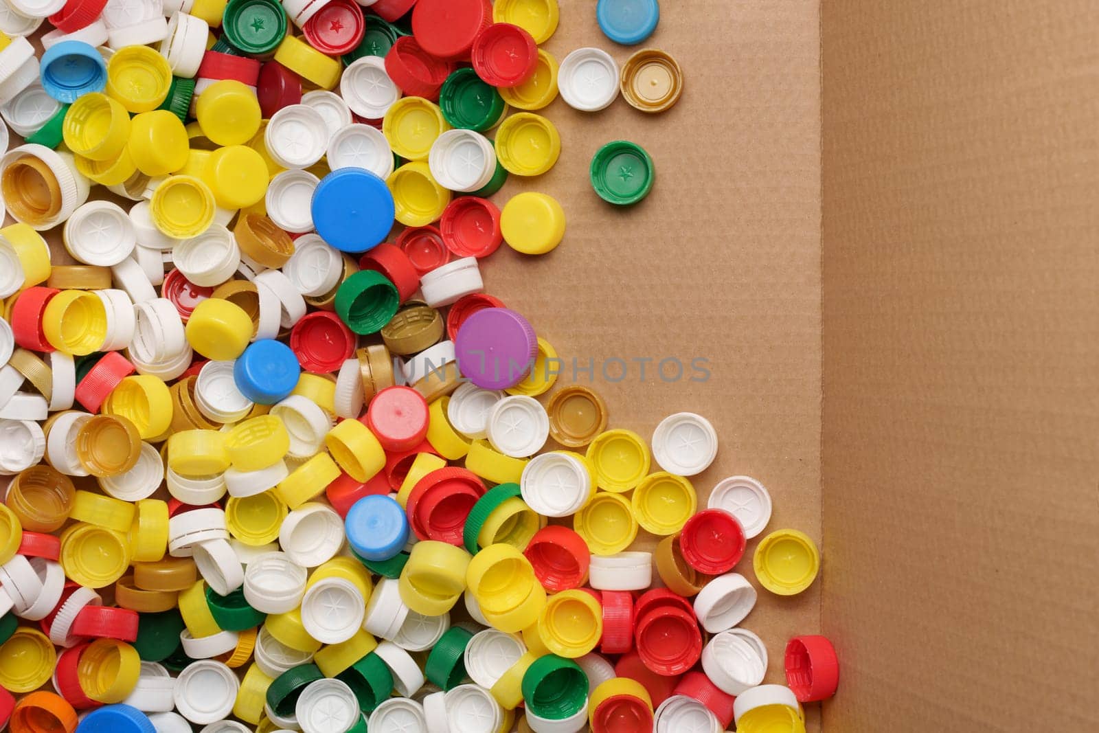Used PET recycling plastic bottle cap plastic lids. Colorful bottle caps background cardboard box. Garbage PET waste recycling bottle cap sorting waste plastic garbage collection. Recyclable materials by synel