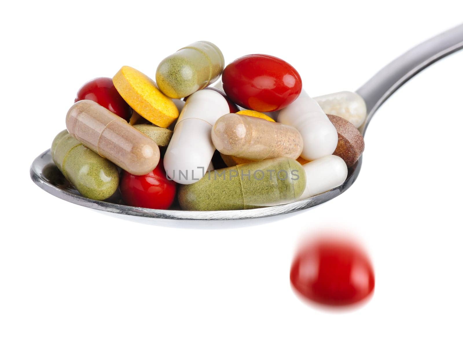 Spoon overflowing with tablets,a tablet falling down,white background