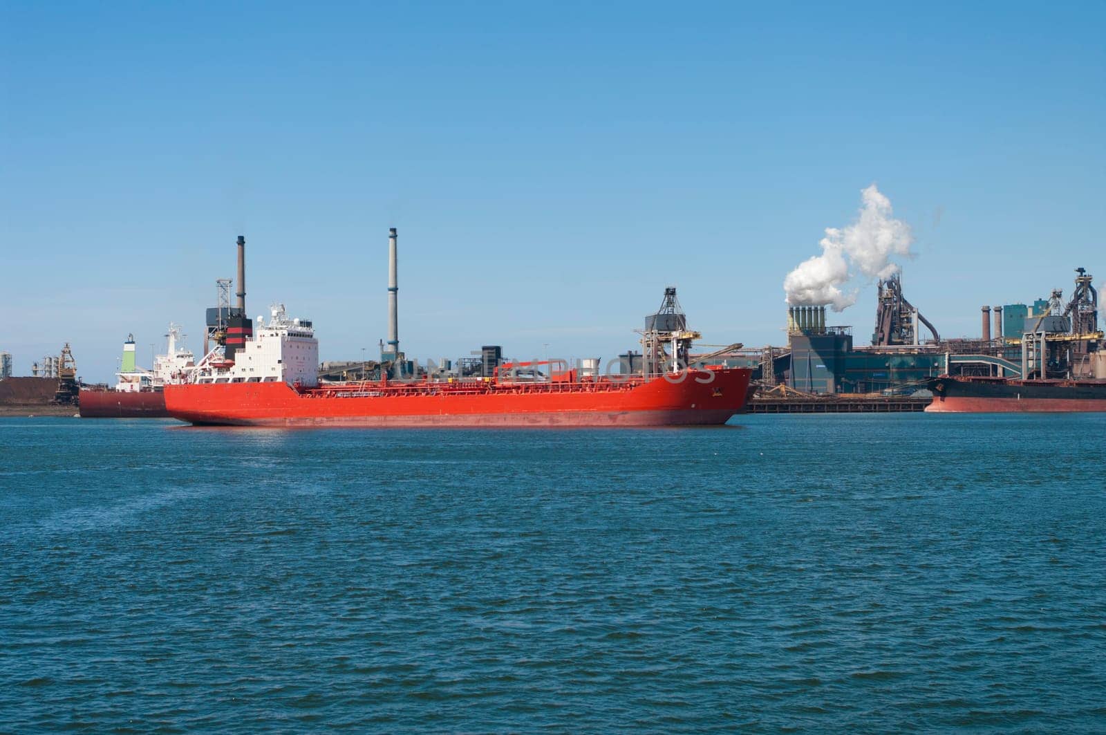 red tanker passing by a large steel factory in IJmuiden, Netherlands