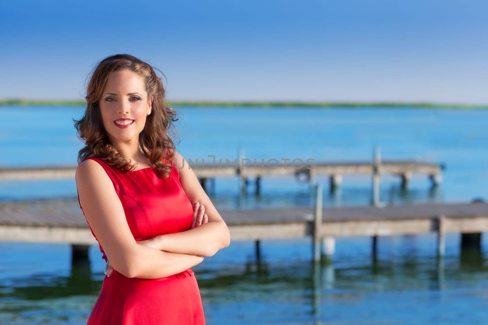 Brunette woman dress in red smiling relaxed on a blue lake jetty