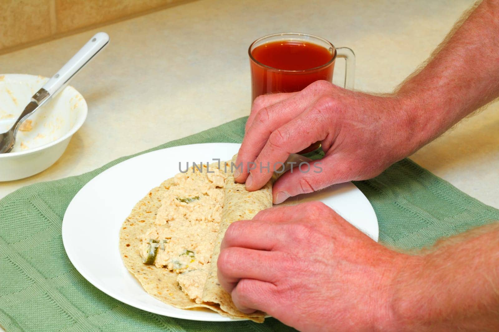 Male hands rolling up salmon salad with jalapenos in a multi-grain soft tortilla for lunch.