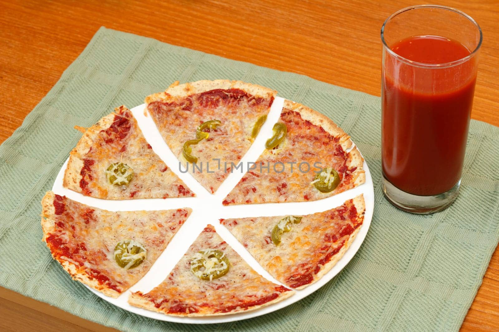Sliced thin crust tortilla pizza topped with tomato paste, mozzarella cheese, jalapenos and pepper along with a tall glass of tomato vegetable juice.