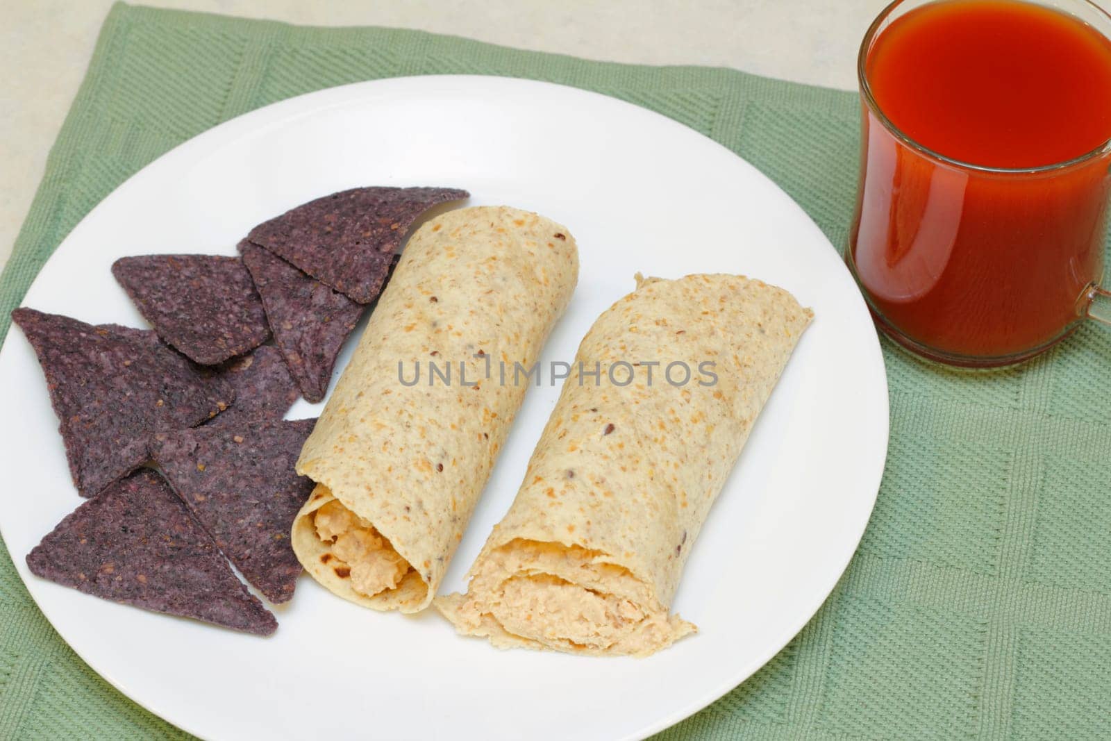 Salmon salad tortilla rolls with blue corn chips on the side as well as a glass of vegetable tomato juice.