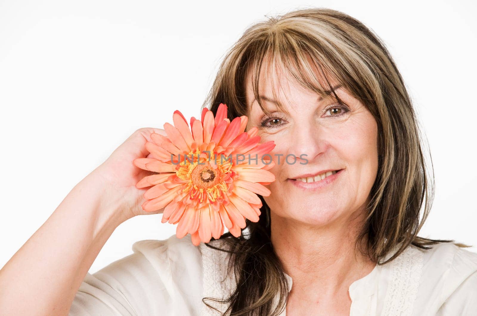Head and shoulders portrait of a middle-aged woman with orange-colored flower against neutral light studio background