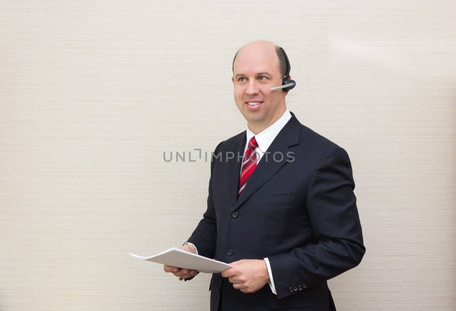 Business man with a handsfree telephone headset holding a document.