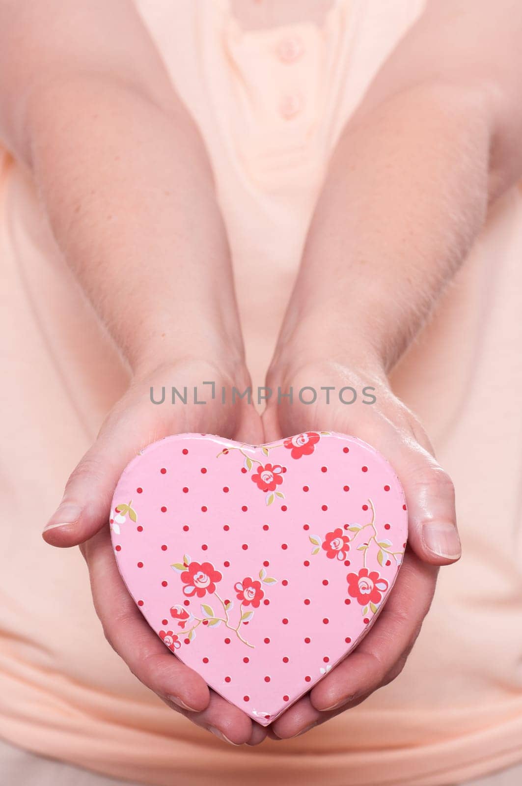 Woman holding a pink heart with flowers and both hands forward