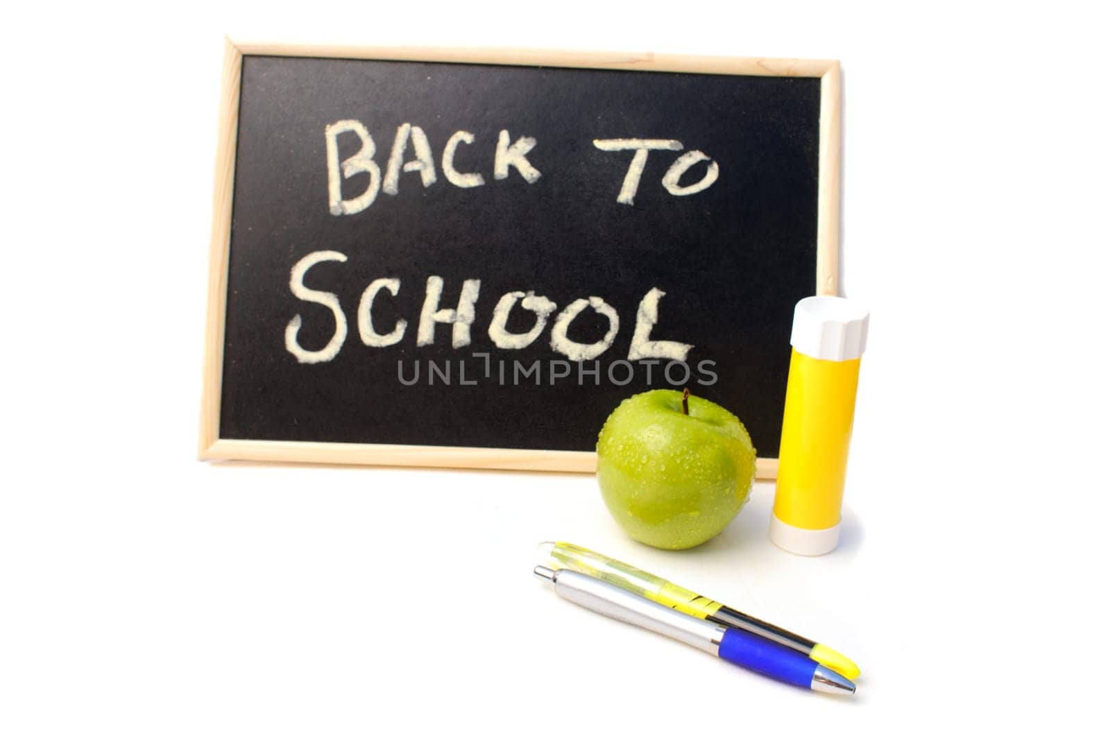 Pens, glue stick and an apple in front of a back to school written on a blackboard