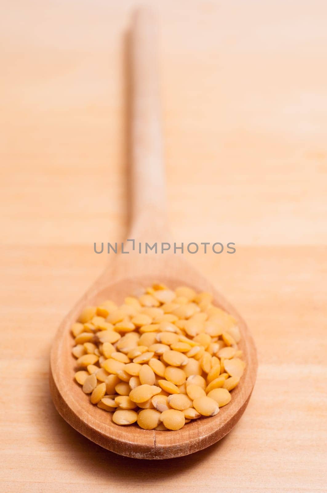 Close-up wooden spoon with yellow lentils in portrait format