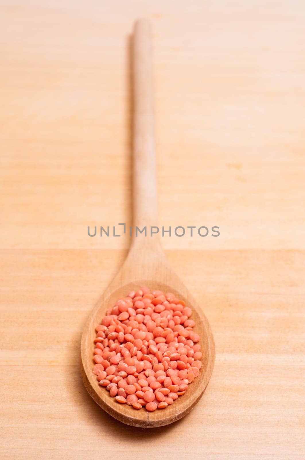 Red lentils on a wooden spoon in portrait format