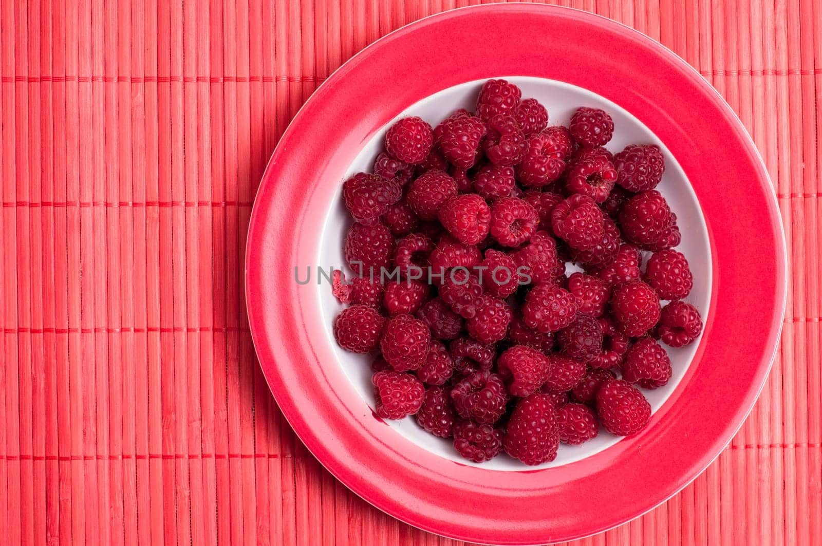 Ripe red raspberries on a red plate
