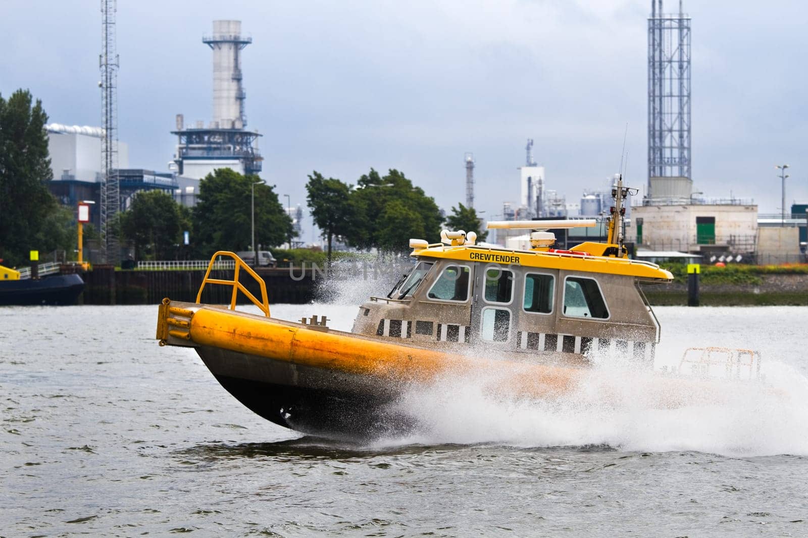 Crewtender passing by at full speed in port - with industrial background and rainy sky