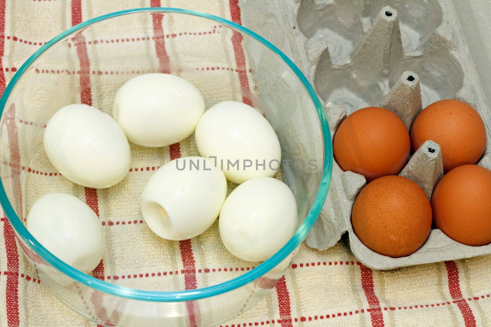 Six boiled eggs in a glass bowl next to four organic brown eggs in an egg carton.