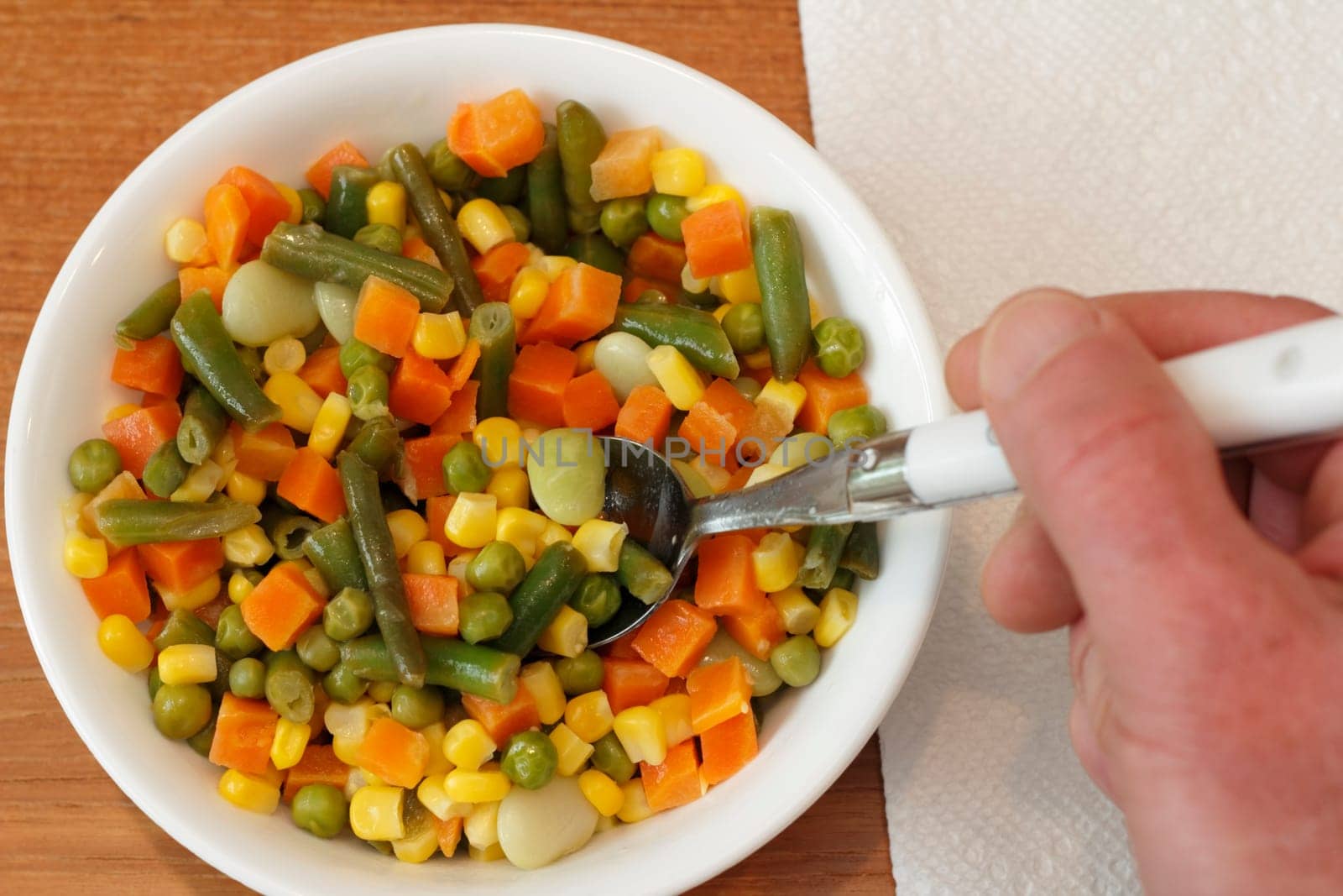 White bowl of mixed vegetables about to be eaten with spoon in hand.