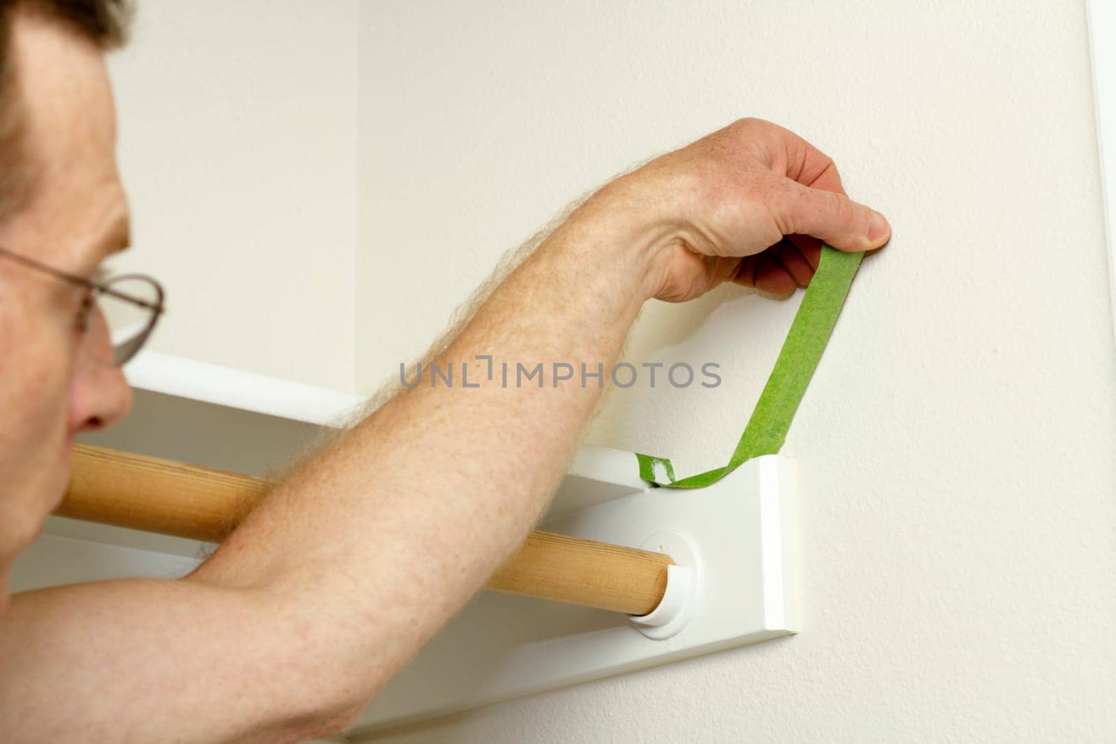 Having finished painting the walls of a closet a man removes the green painter&#039 s tape from around the shelf he was protecting.