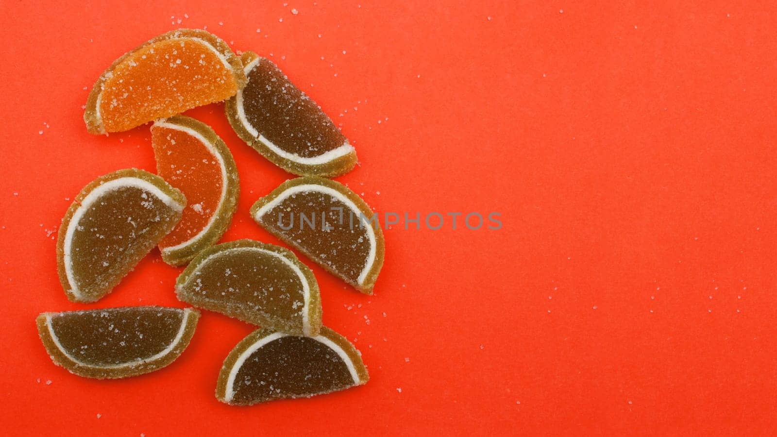 Green and red slices of marmalade on a red background, copy space, top view.