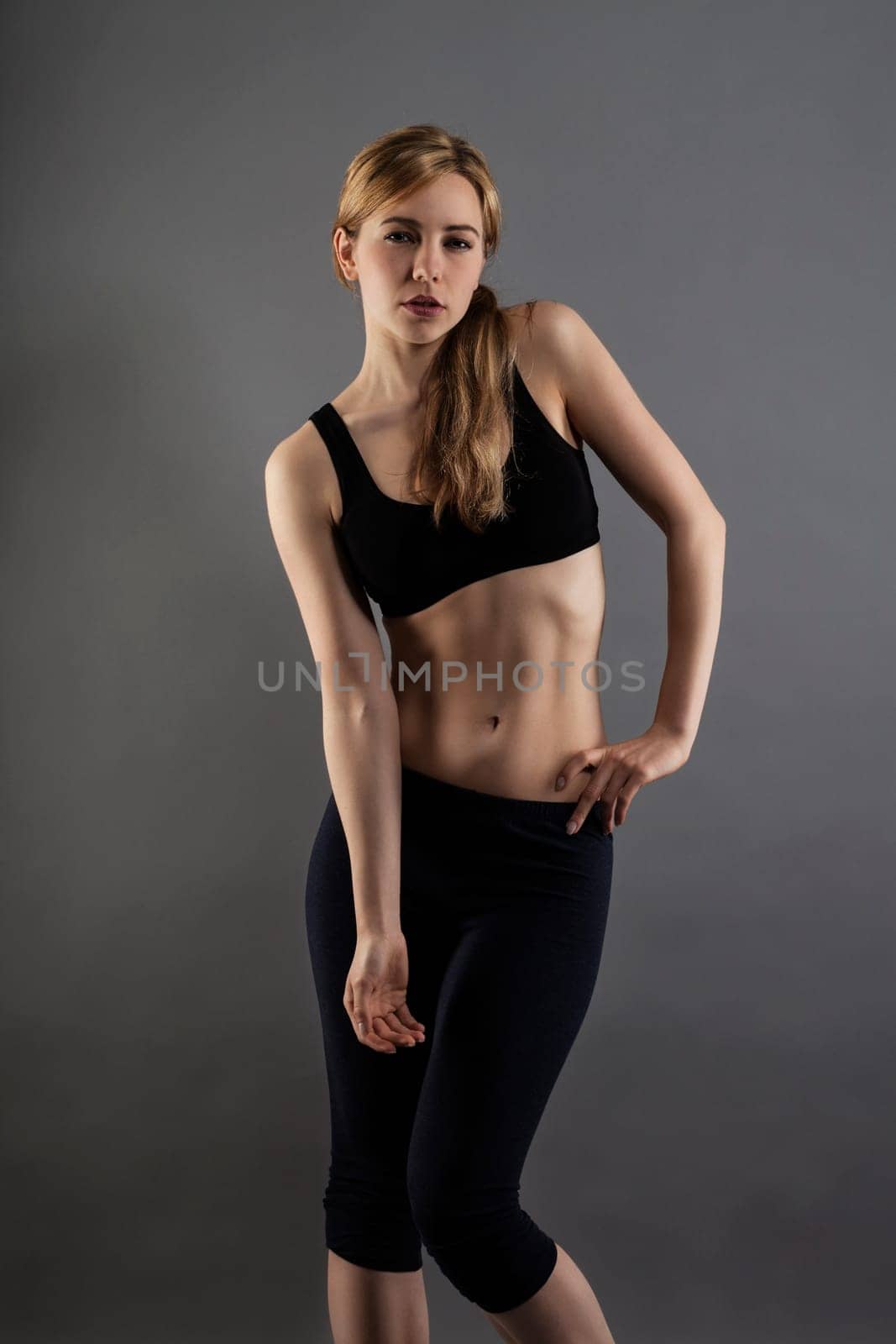Beautiful sportswoman in black sports dress against gray background