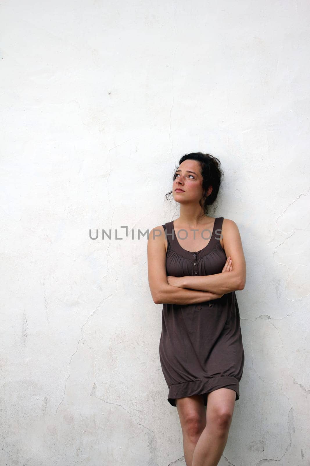 young woman on a plain wall looks pensive