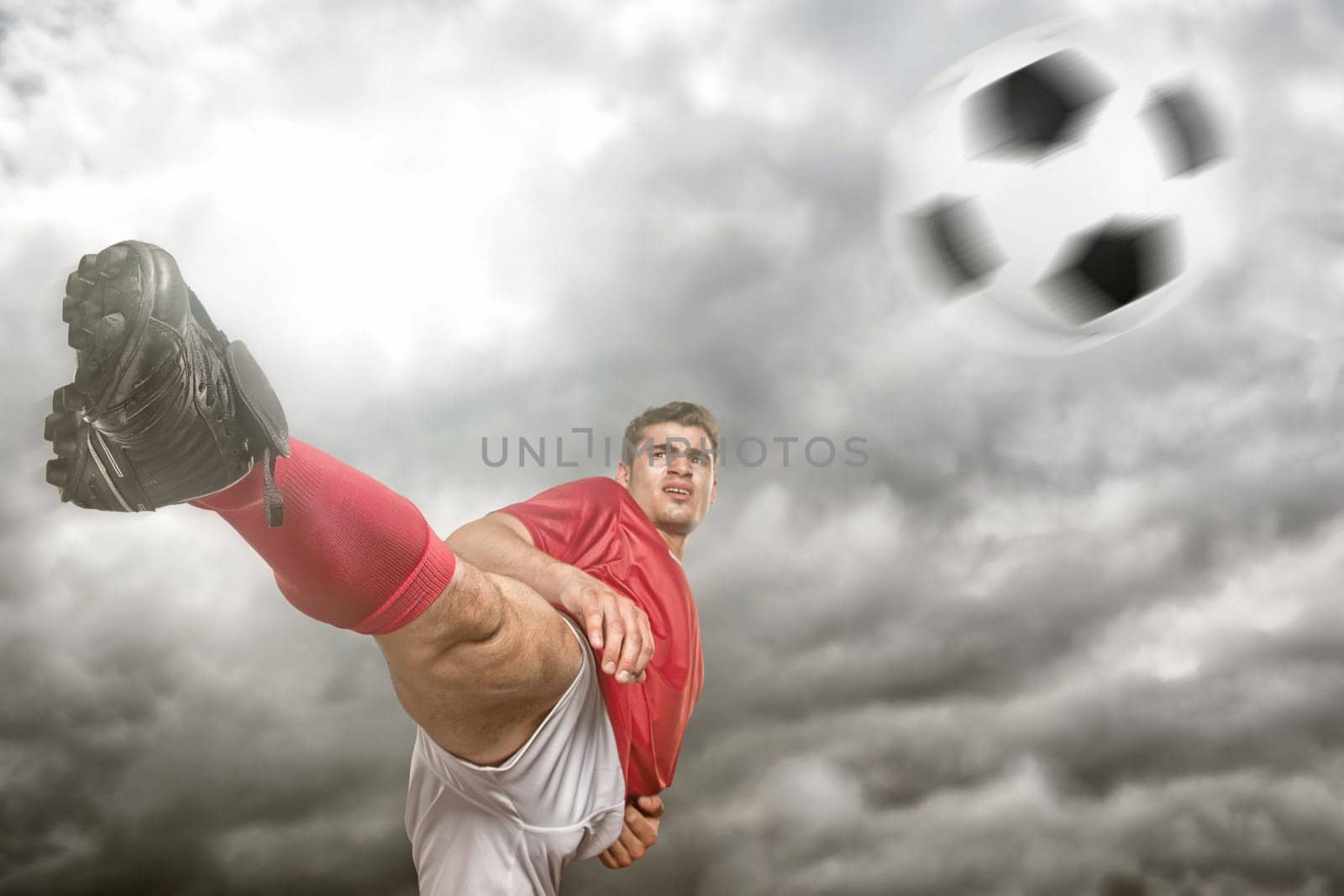 Young soccer player kicks a ball in front of dramatic sky