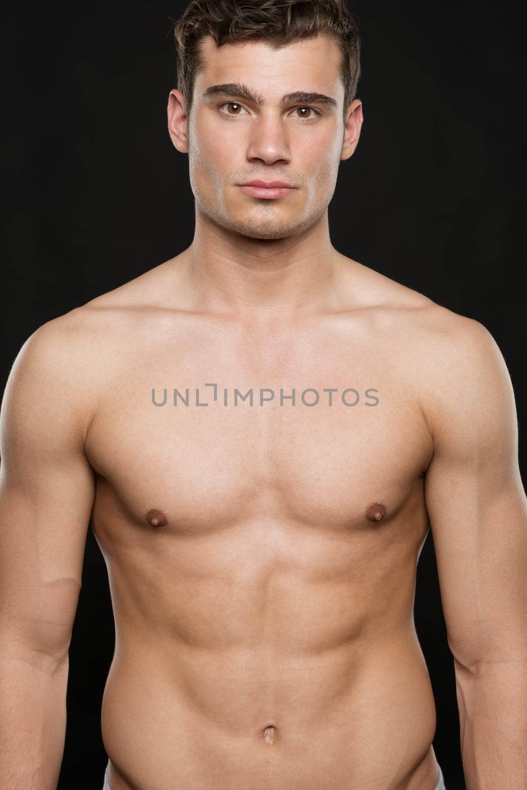 Young shirtless man against black studio background