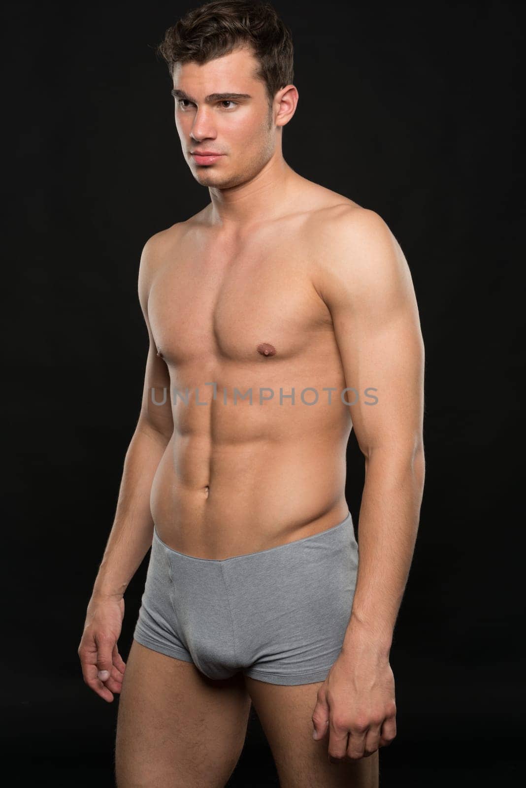 Young shirtless man against black studio background