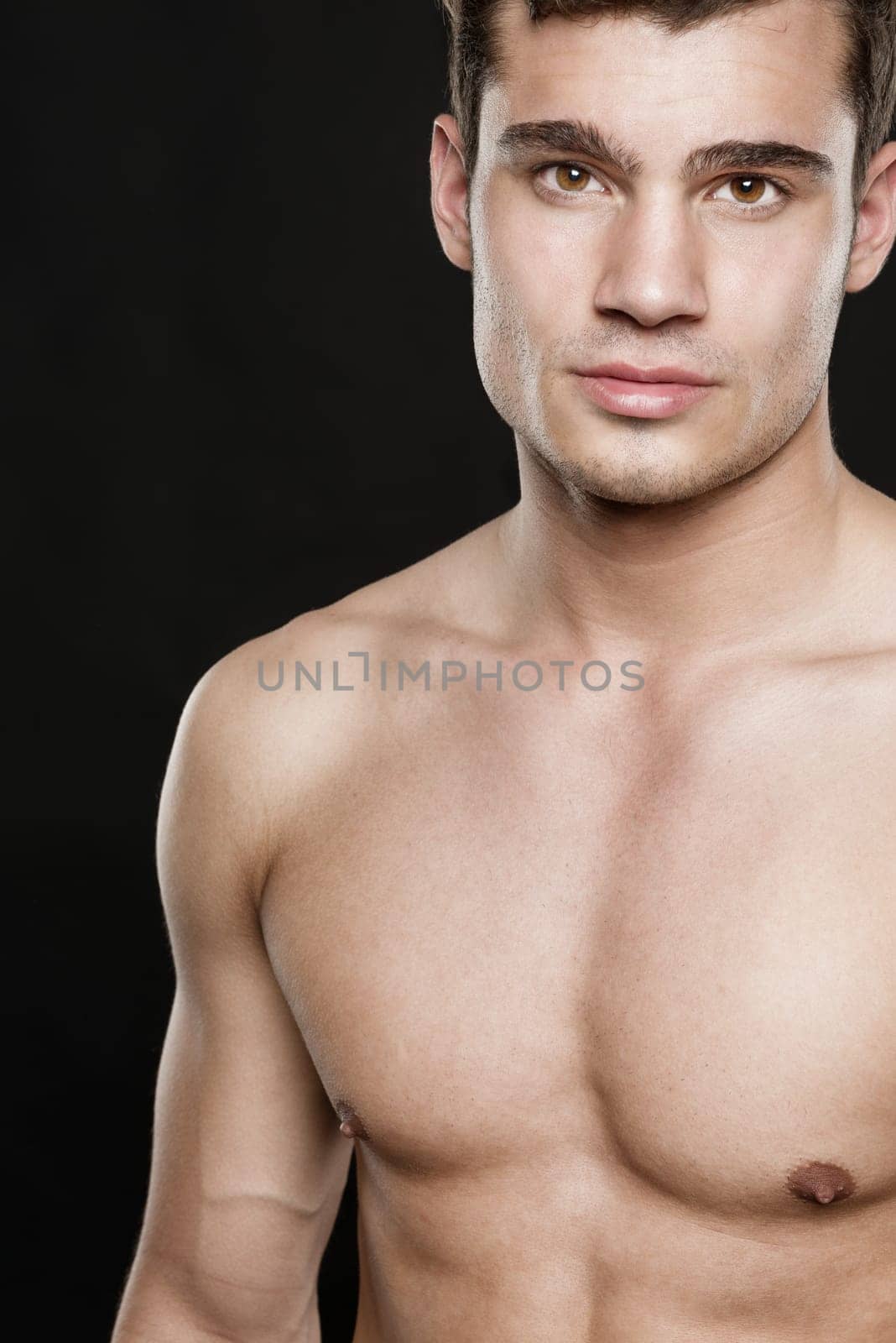 Young shirtless man against black studio background