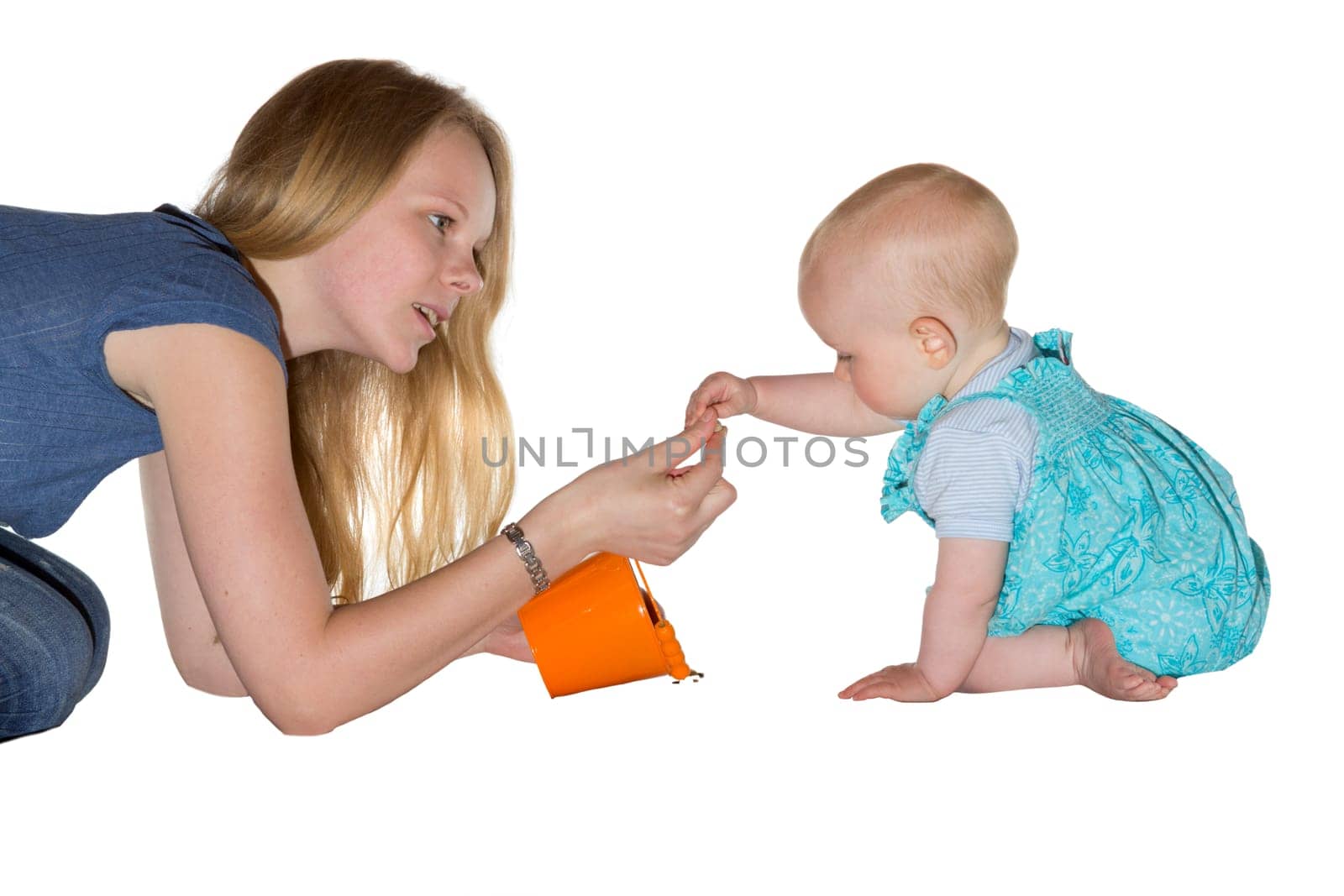 Young mother kneeling on the floor giving a treat to her adorable small baby who is carefully taking it from her hand