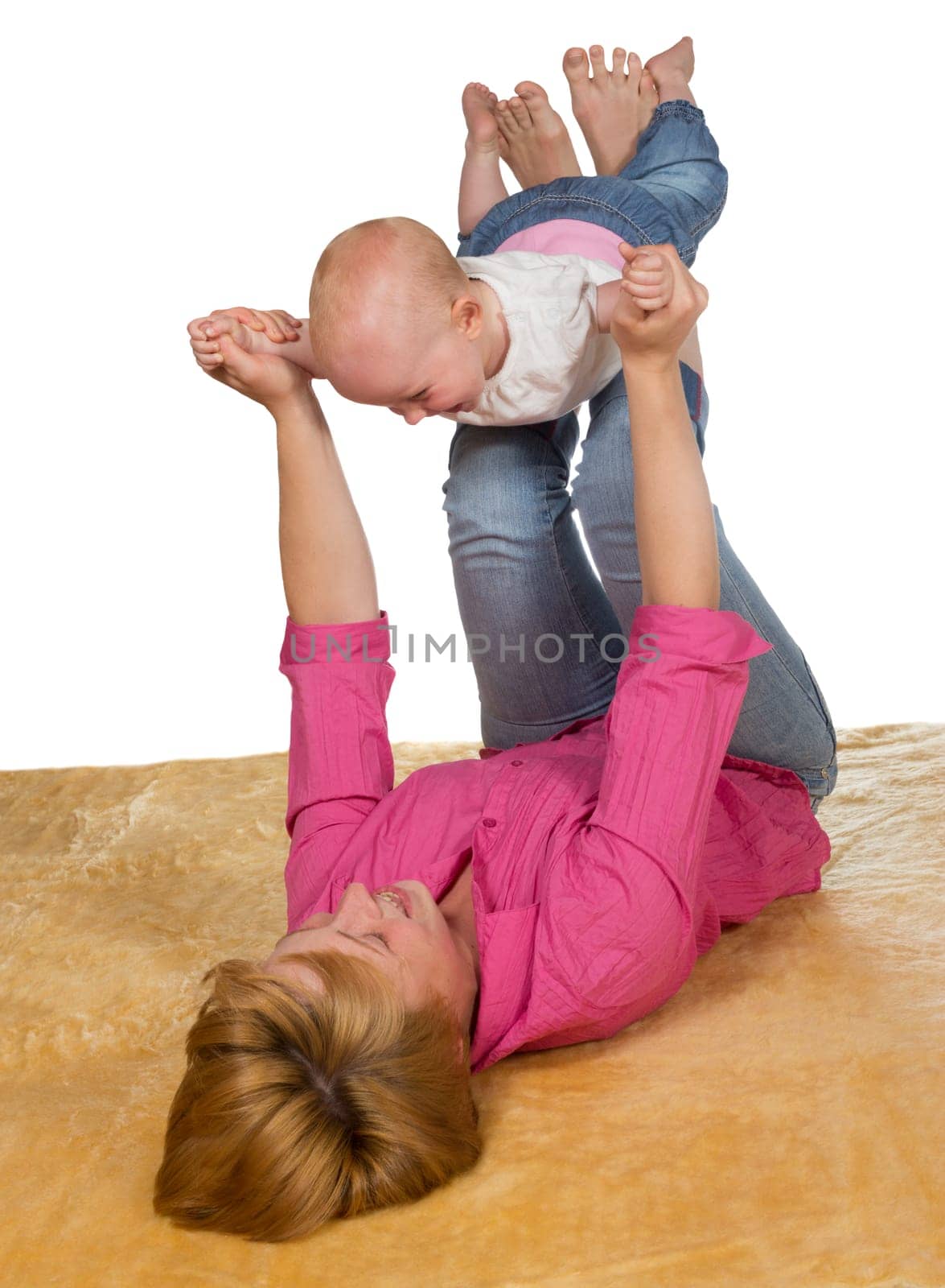 Young mother lying on her back on the floor playing with her baby which is balanced on her raised legs with its arms outstretched