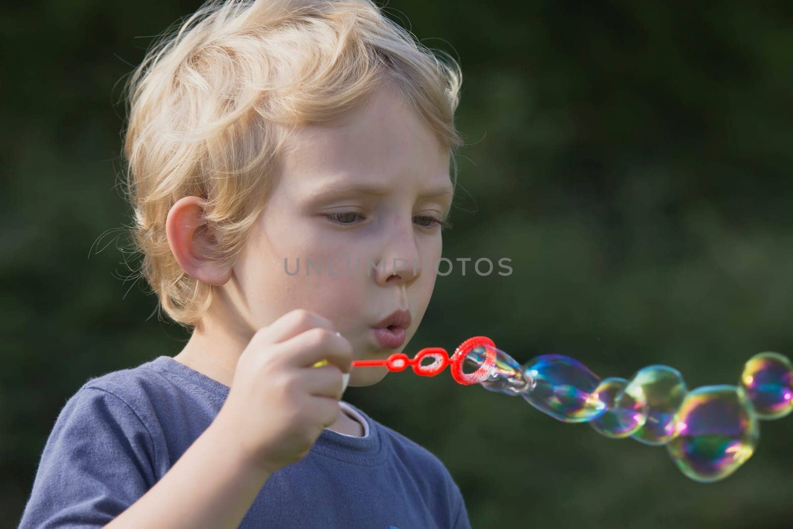 Side view of a blond boy who blows soap bubbles.