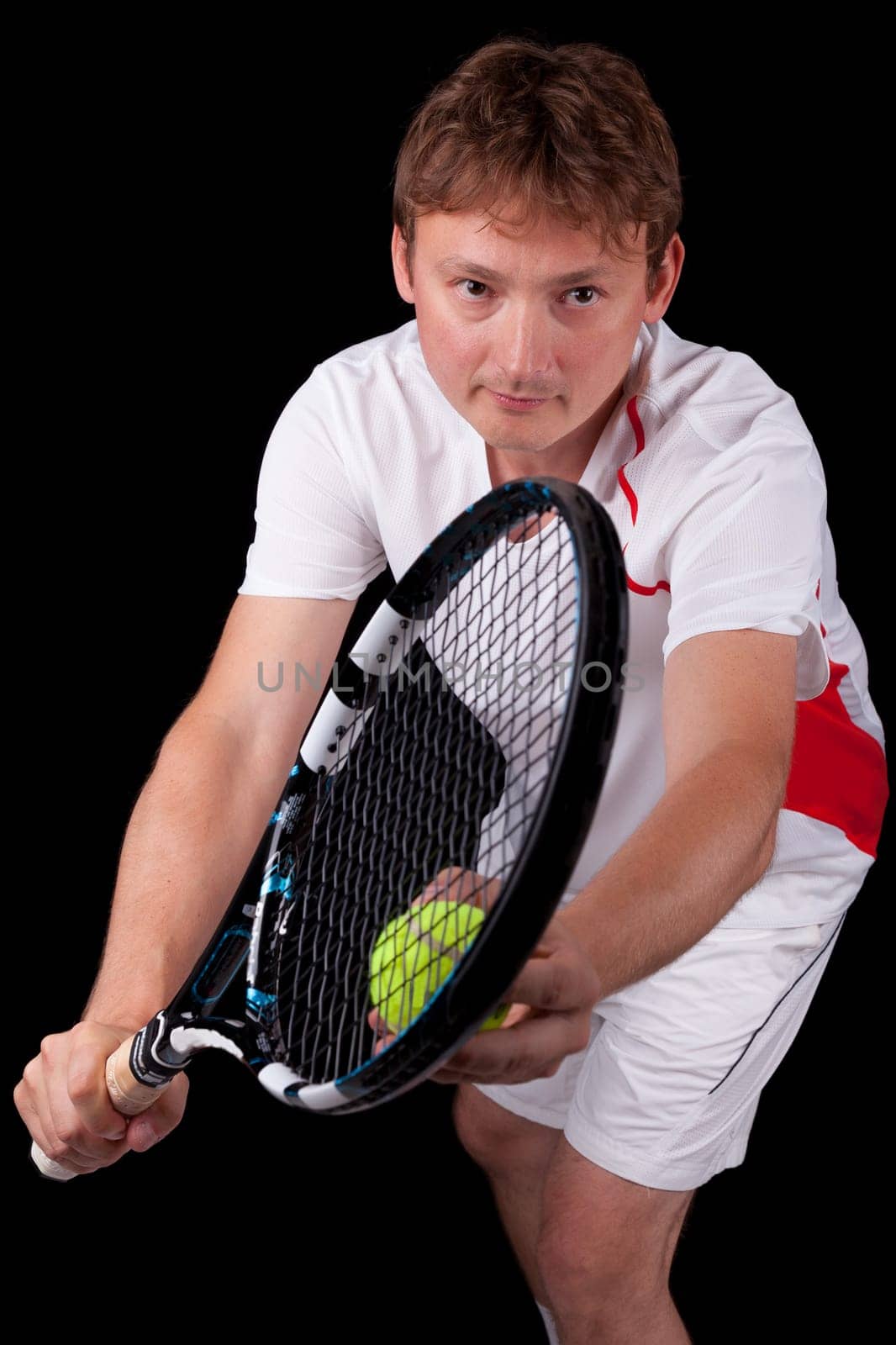 Portrait of a young male tennis player about to serve the ball, over black background