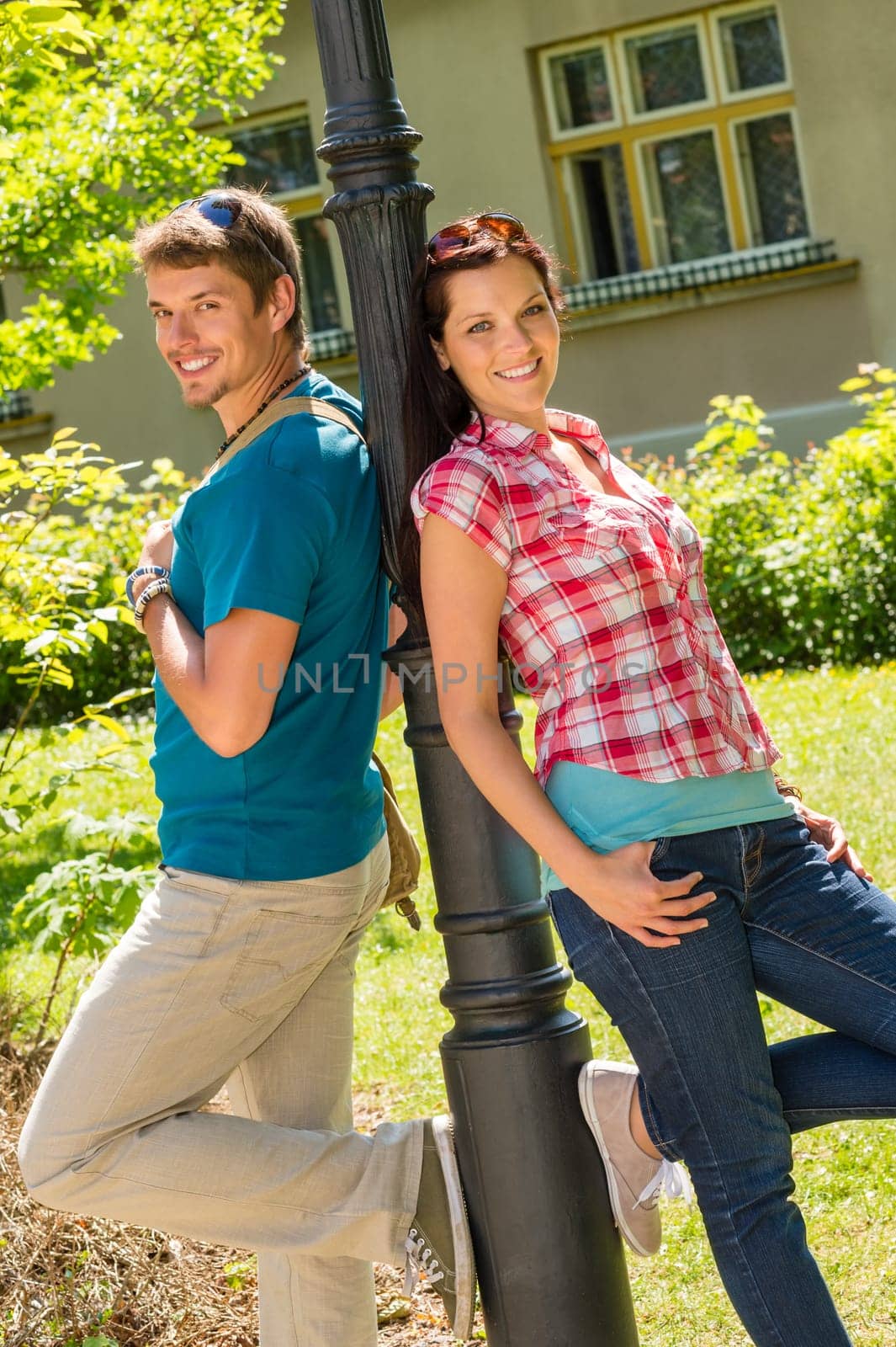 Young couple in love lean against city lamp sunny park