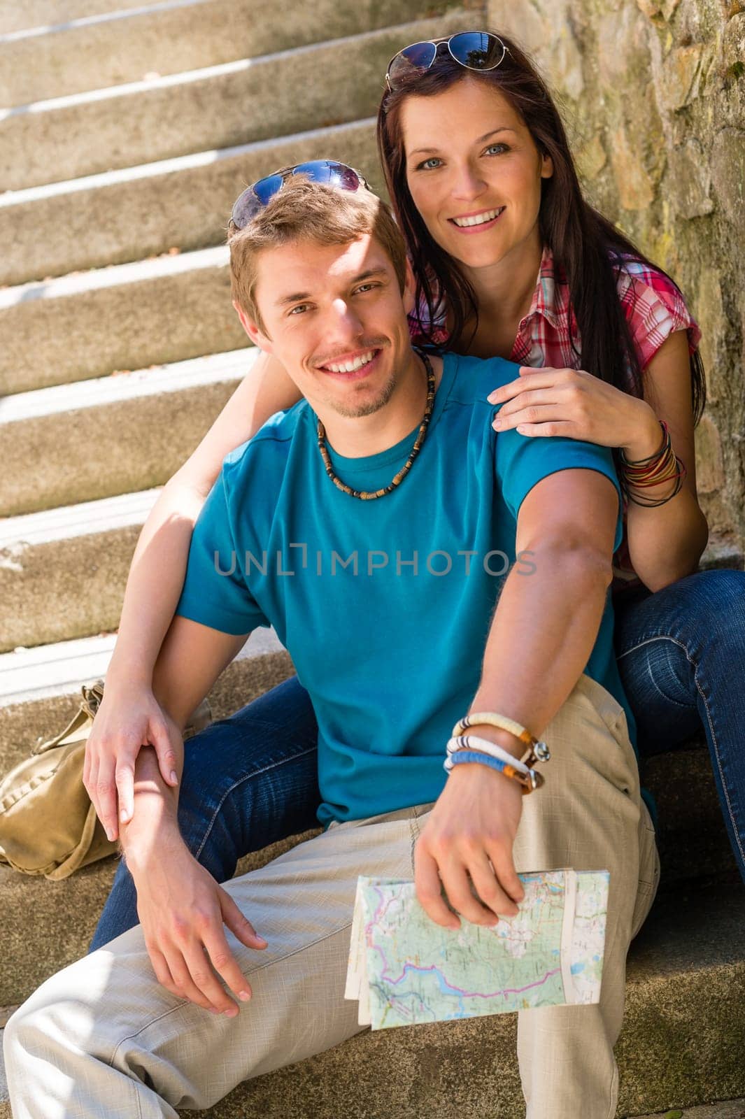 Happy young couple sitting on stairs smiling holding city map