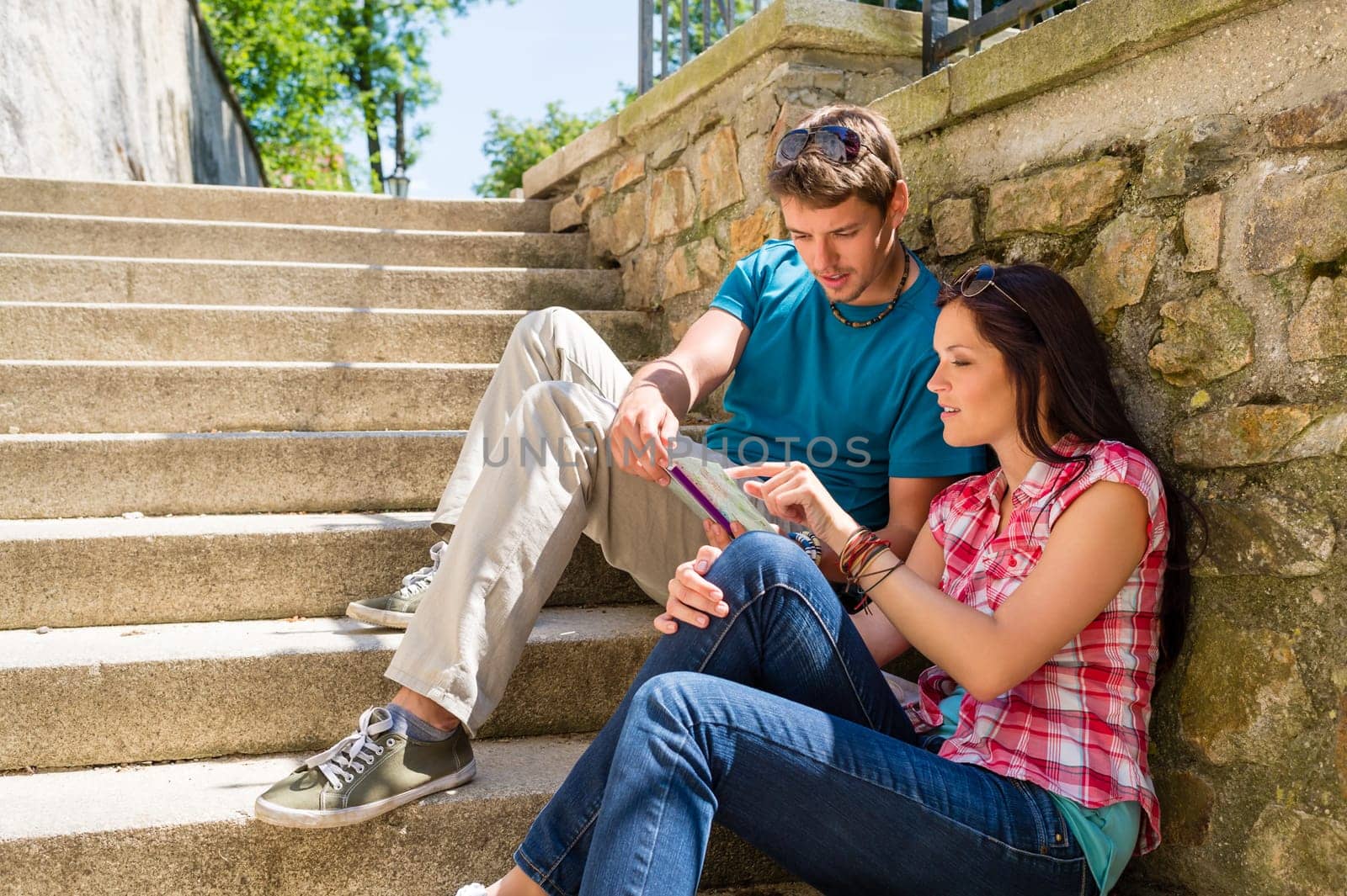Young couple looking city map sunny day sitting stairs together