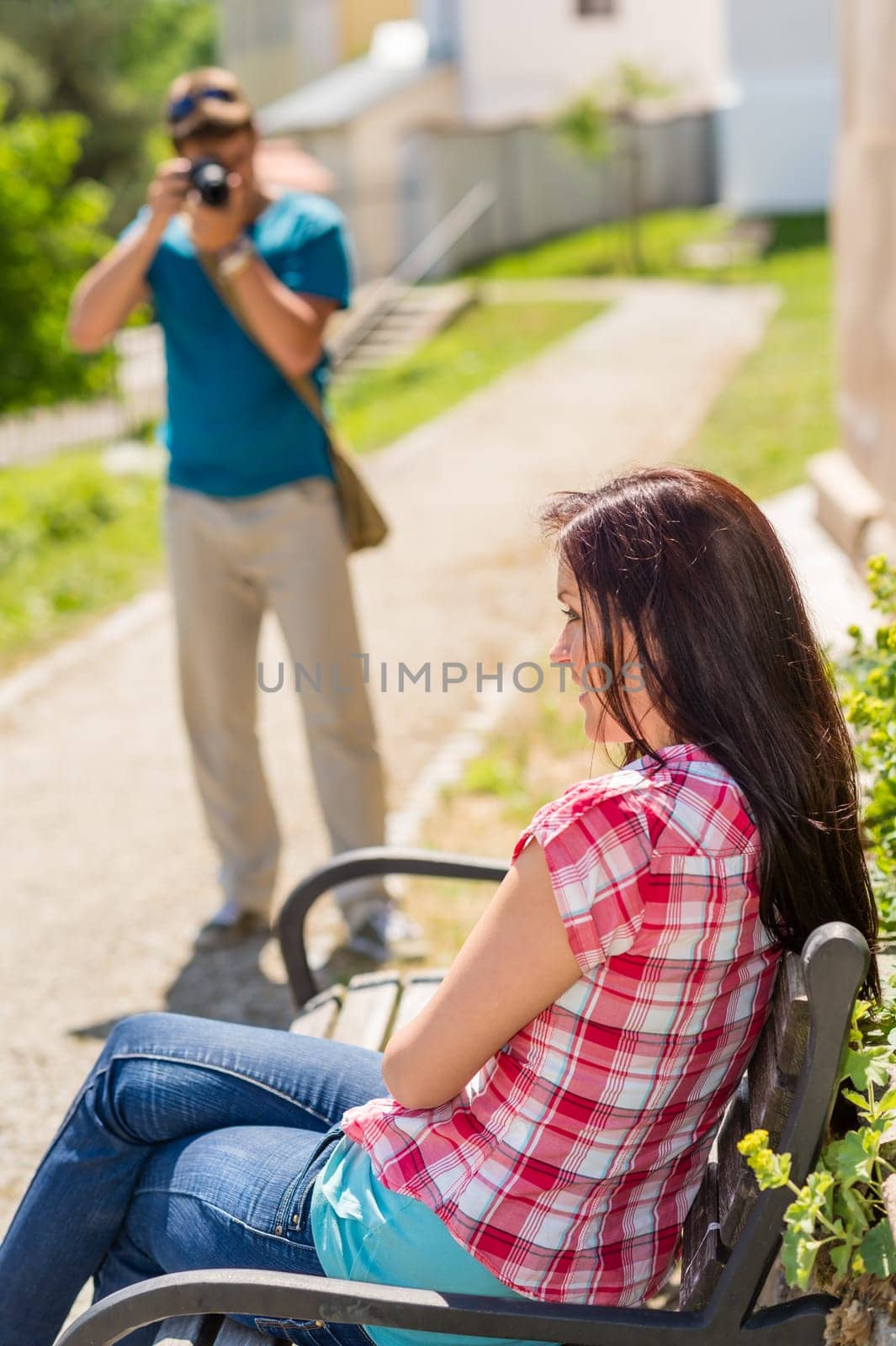 Young man take photo of his girlfriend sitting park bench