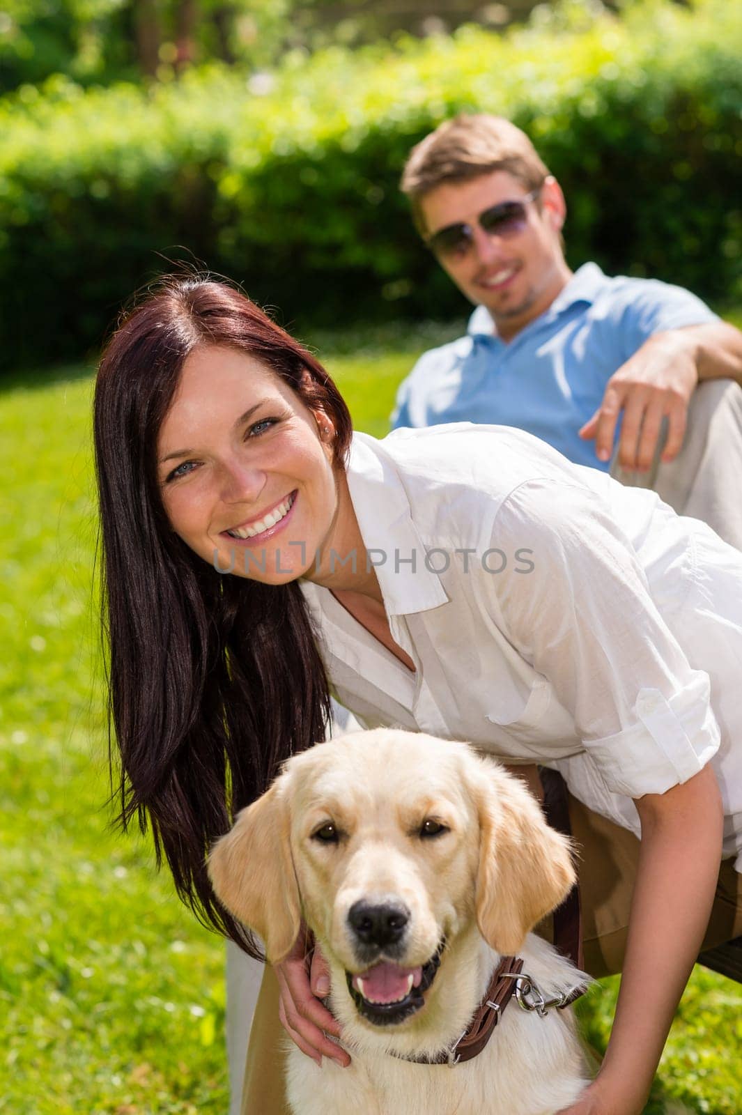 Happy young couple sitting with golden retriever dog in park
