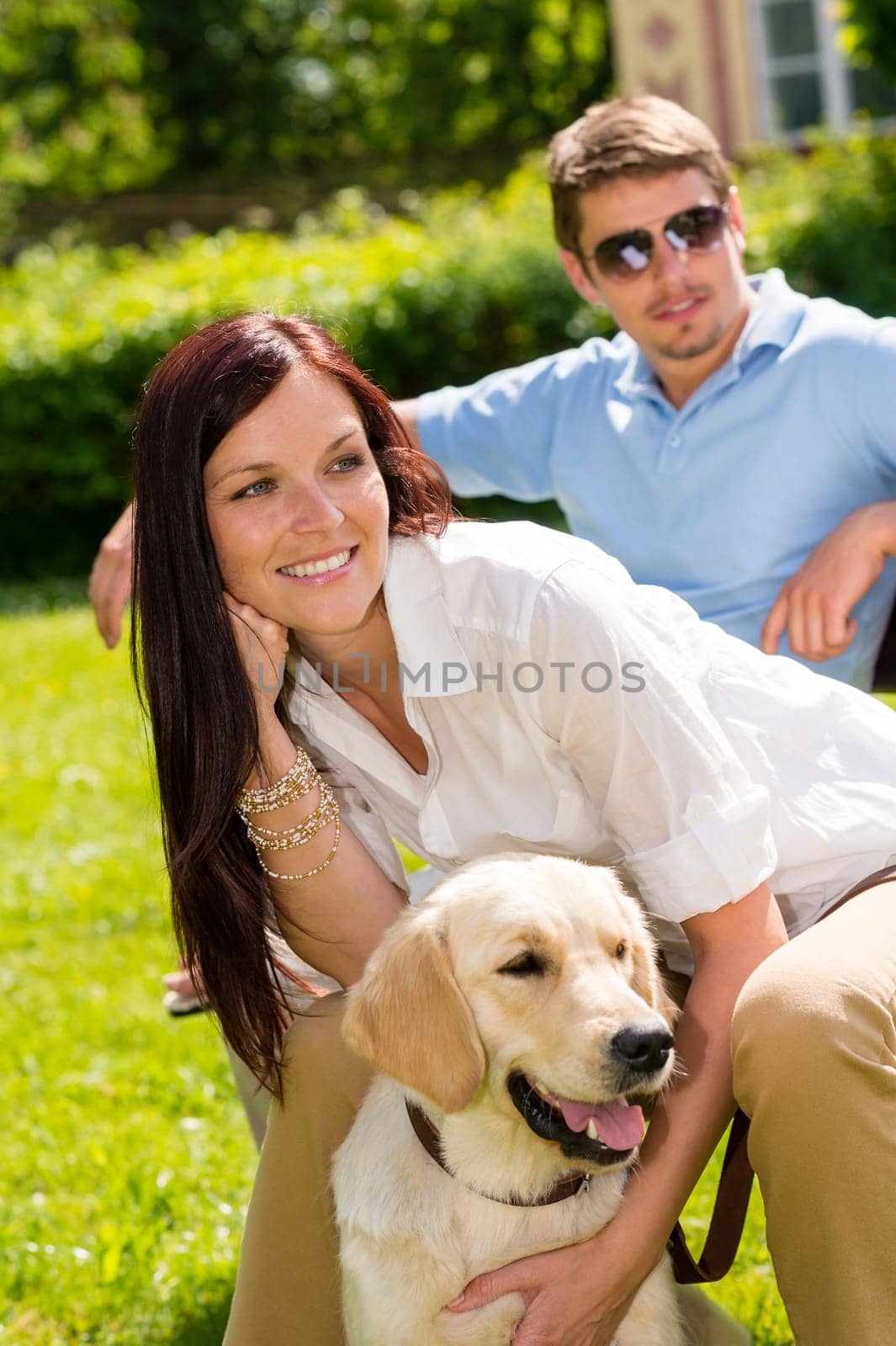 Happy young couple sitting with golden retriever dog in park