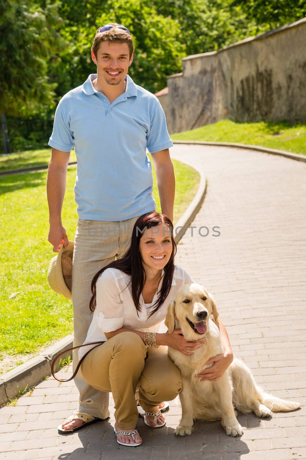 Happy young couple with dog posing on sunny park alley