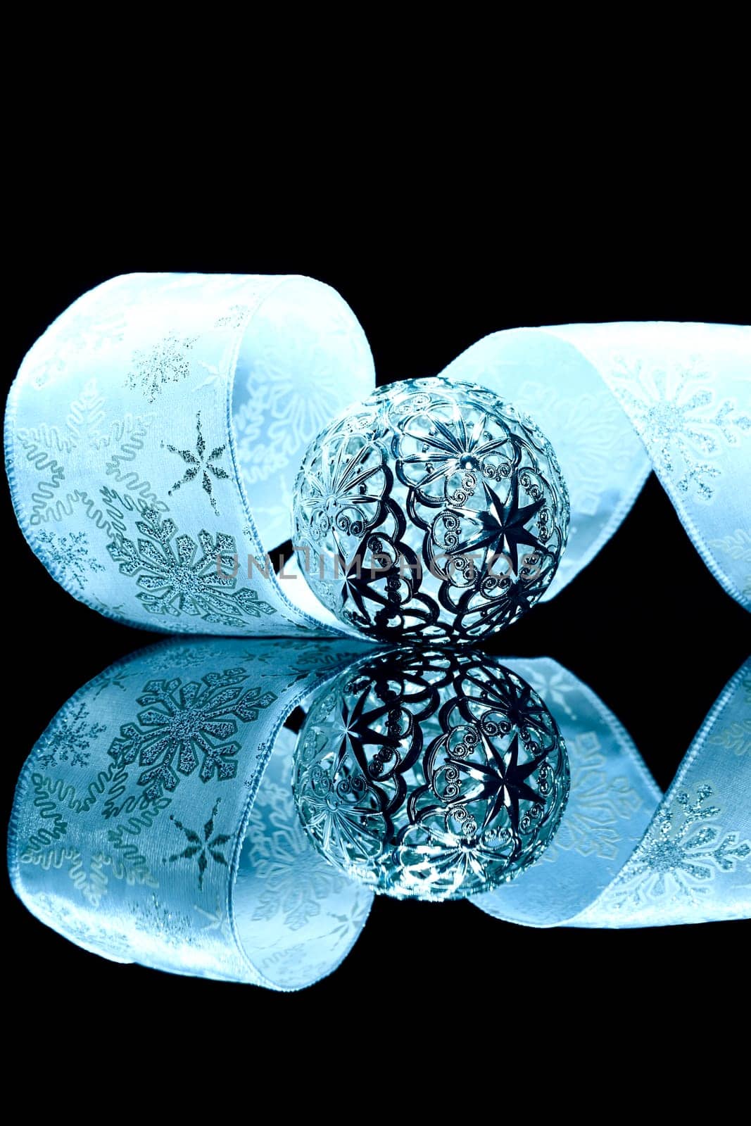 Metal Christmas Ornament in Front of Blue Ribbon on Black Mirror